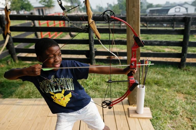 young boy shooting archery at camp