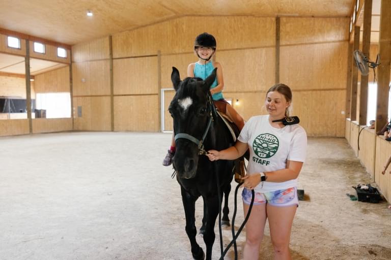 camp child riding horse with camp counselor leading